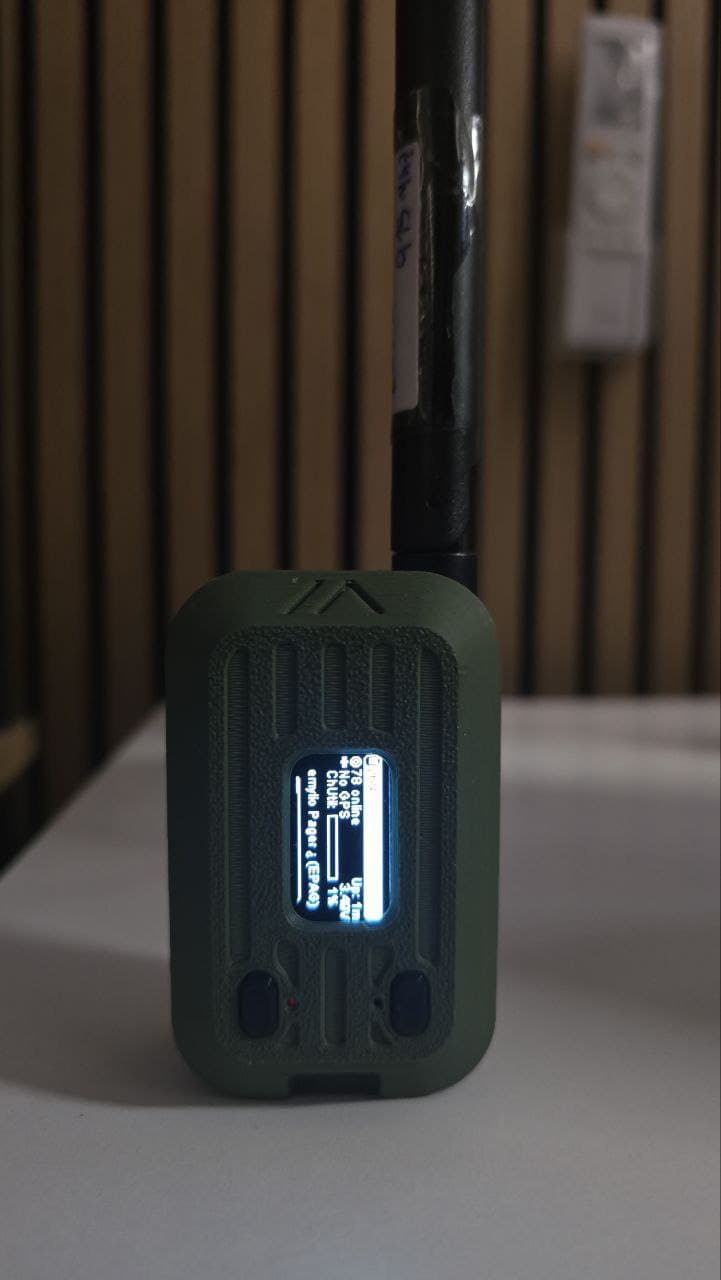 Pager Meshtastic verde con pantalla OLED y antena, mostrando el estado de la red